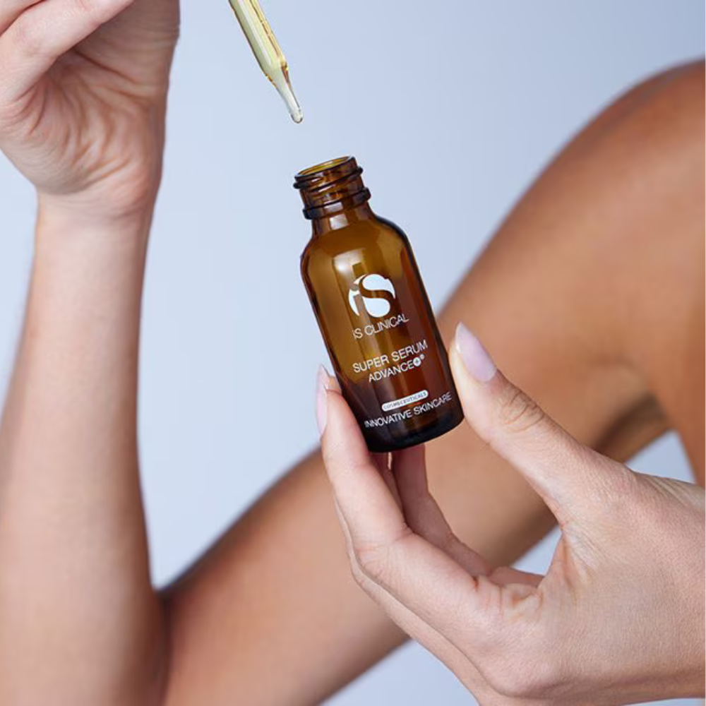 Person holding a brown serum bottle with a dropper, against a light blue background of iS Clinical Super Serum Advance+