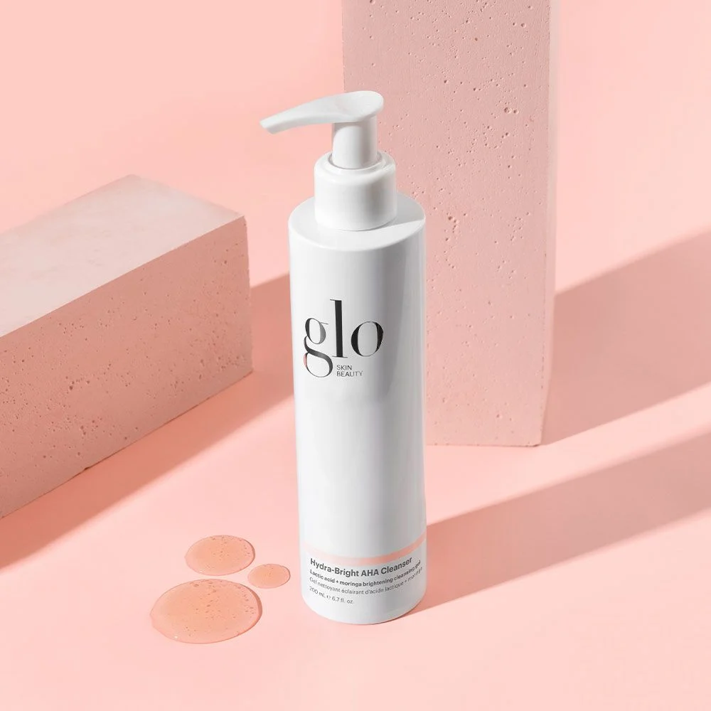 White bottle with pump Glo Skin Beauty Hydra-Bright AHA Cleanser on a pink background