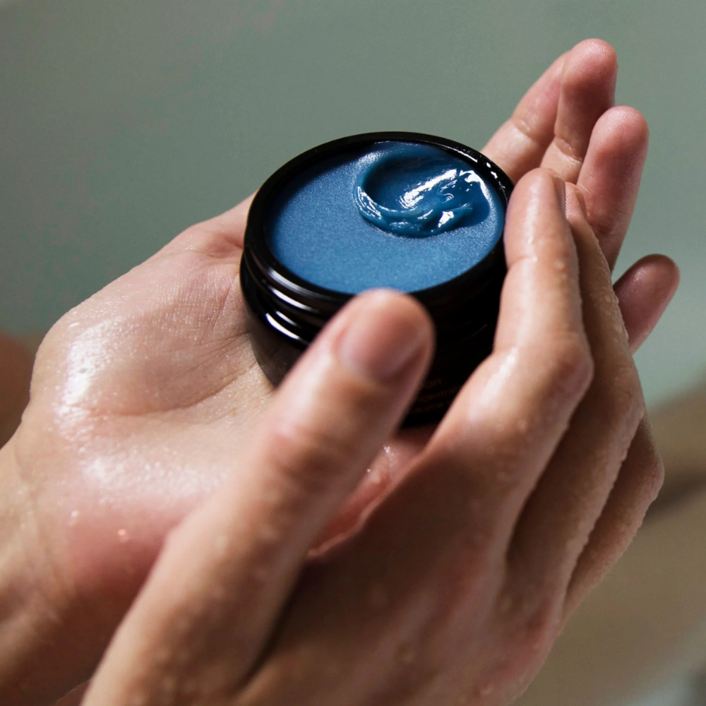 Hand holding a small container May Lindstrom The Blue Cocoon against a neutral background