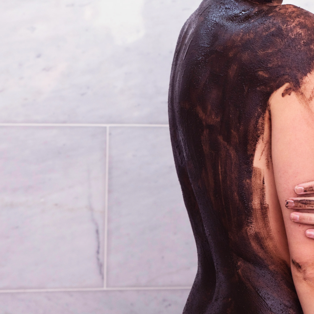 Person with black mud mask on their back and shoulders against a tiled wall