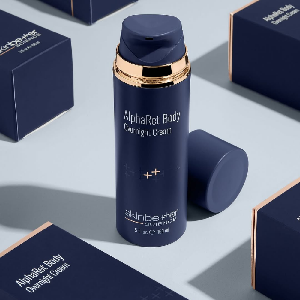 Blue skincare bottle labeled 'Skin Better AlphaRet Body Overnight Cream' with boxes in the background on a light blue surface