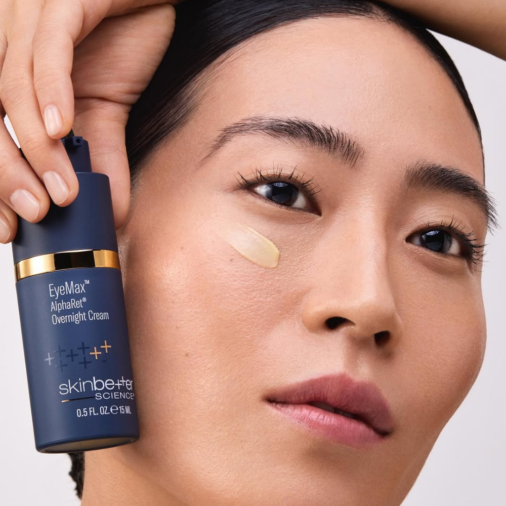 Woman applying skincare cream with a bottle labeled Skin Better EyeMax AlphaRet Overnight Creamscience.