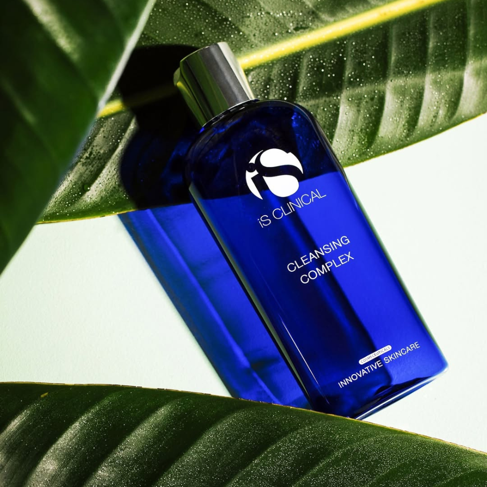 Blue bottle of IS CLINICAL Cleansing Complex on green leaves
