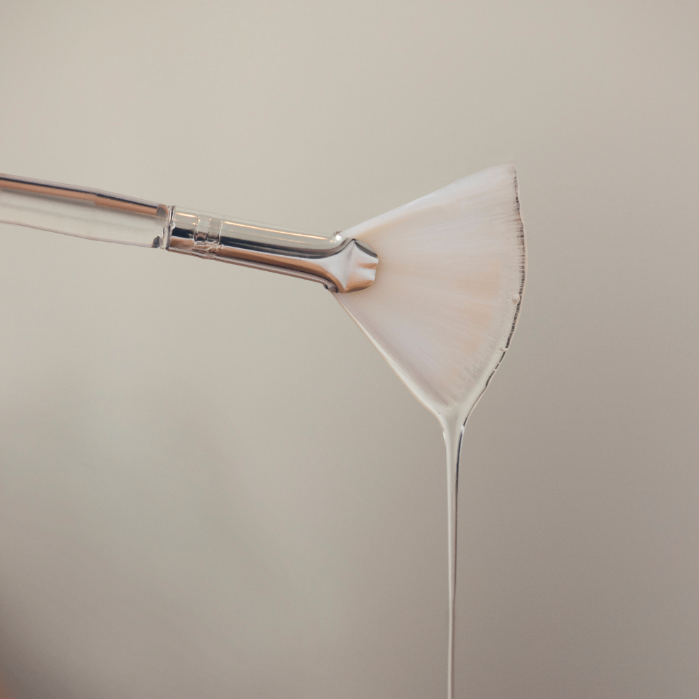 Paintbrush loaded with iS Clinical Cleansing Complex dripping with a white bristle head on a beige background