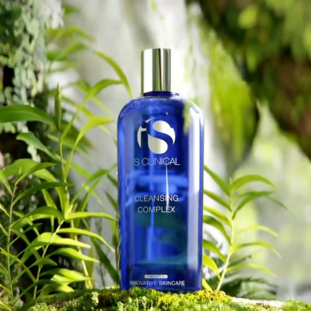 Blue bottle of IS Clinical Cleansing Complex with green foliage in the background