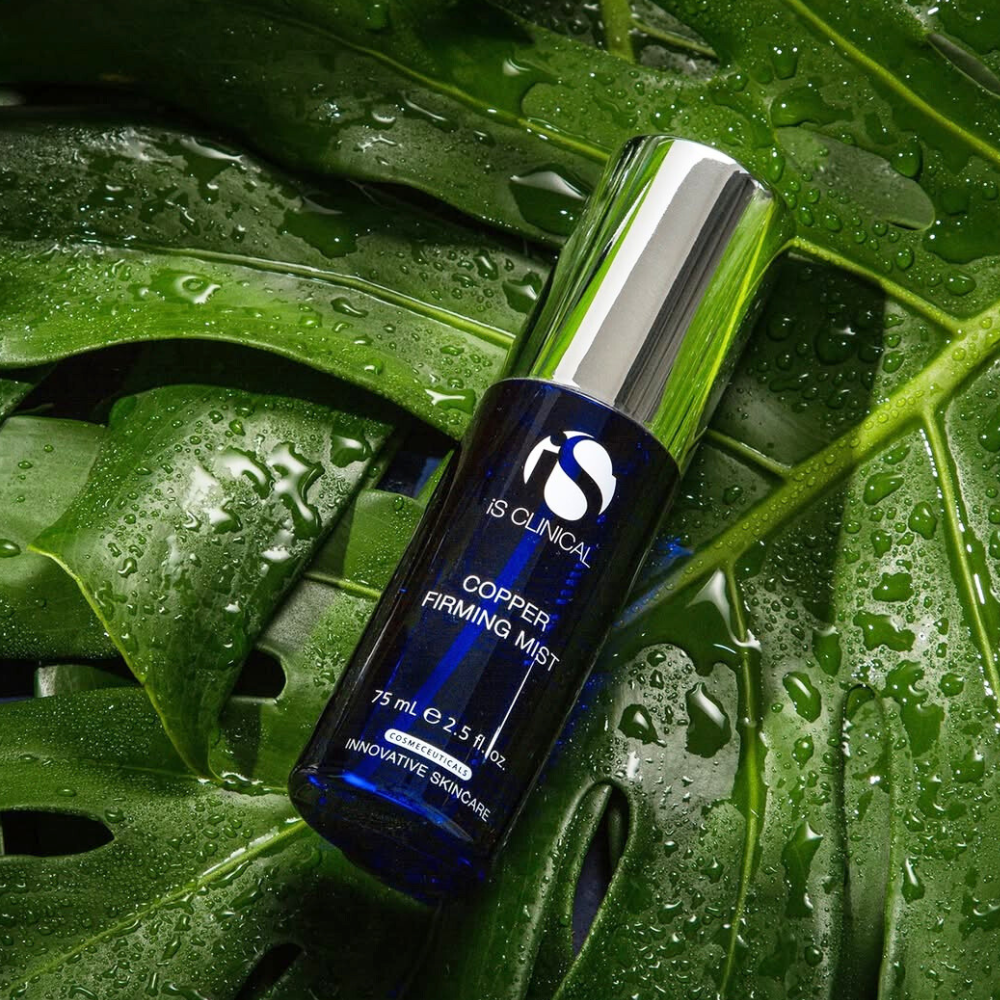 Blue bottle of IS Clinical Copper Firming Mist on green leaves with water droplets.