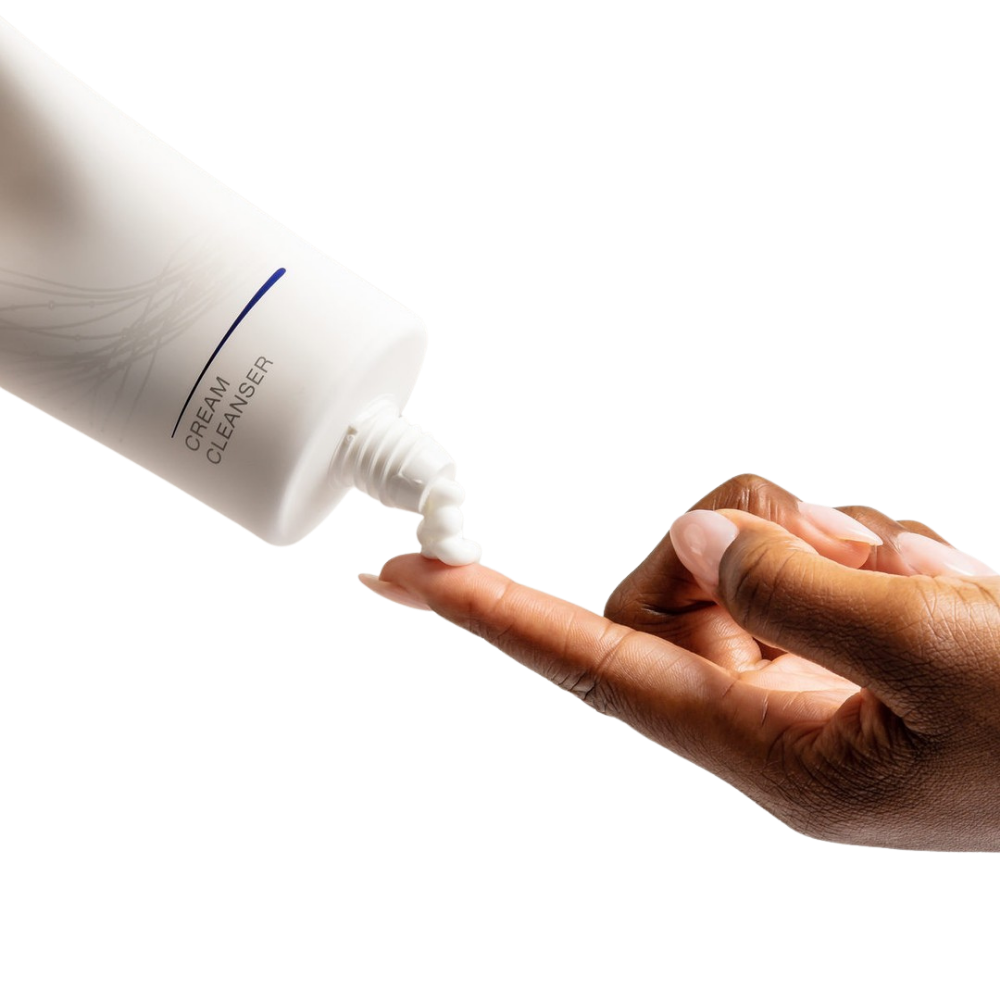 Hand holding a bottle of iS Clinical Cream Cleanser with a close-up of the product on a finger