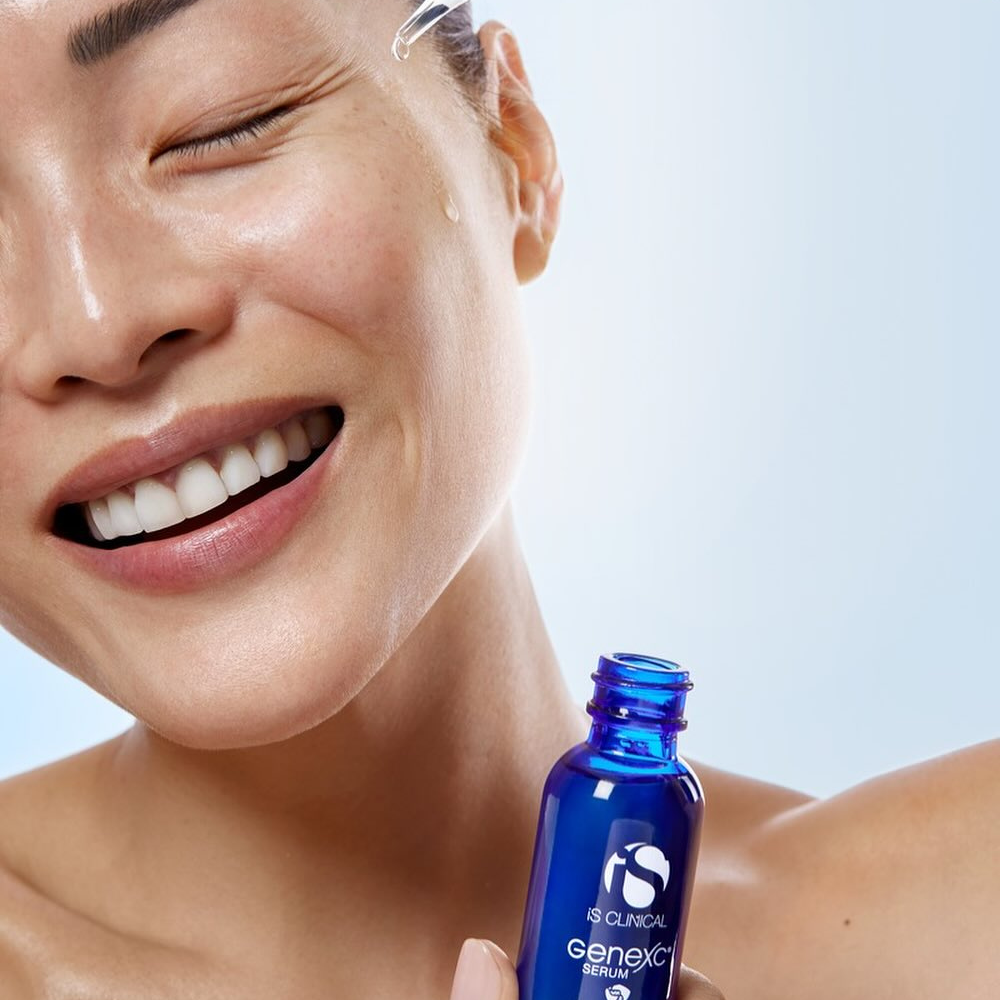 Person holding a blue iS Clinical GeneXC Serum bottle against a light background