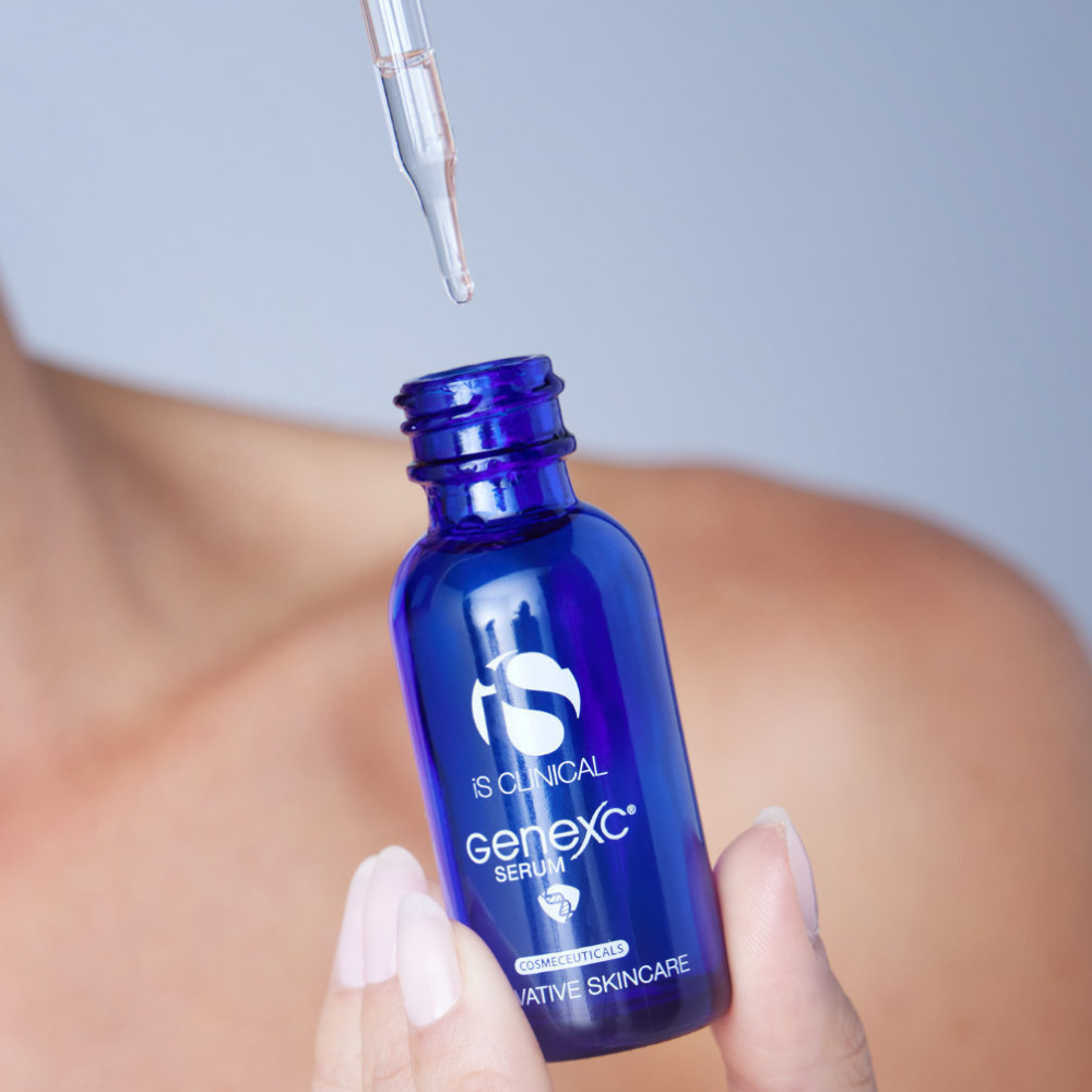 Blue Genexc serum bottle of iS Clinical GeneXC Serum with dropper held by a hand against a blurred background