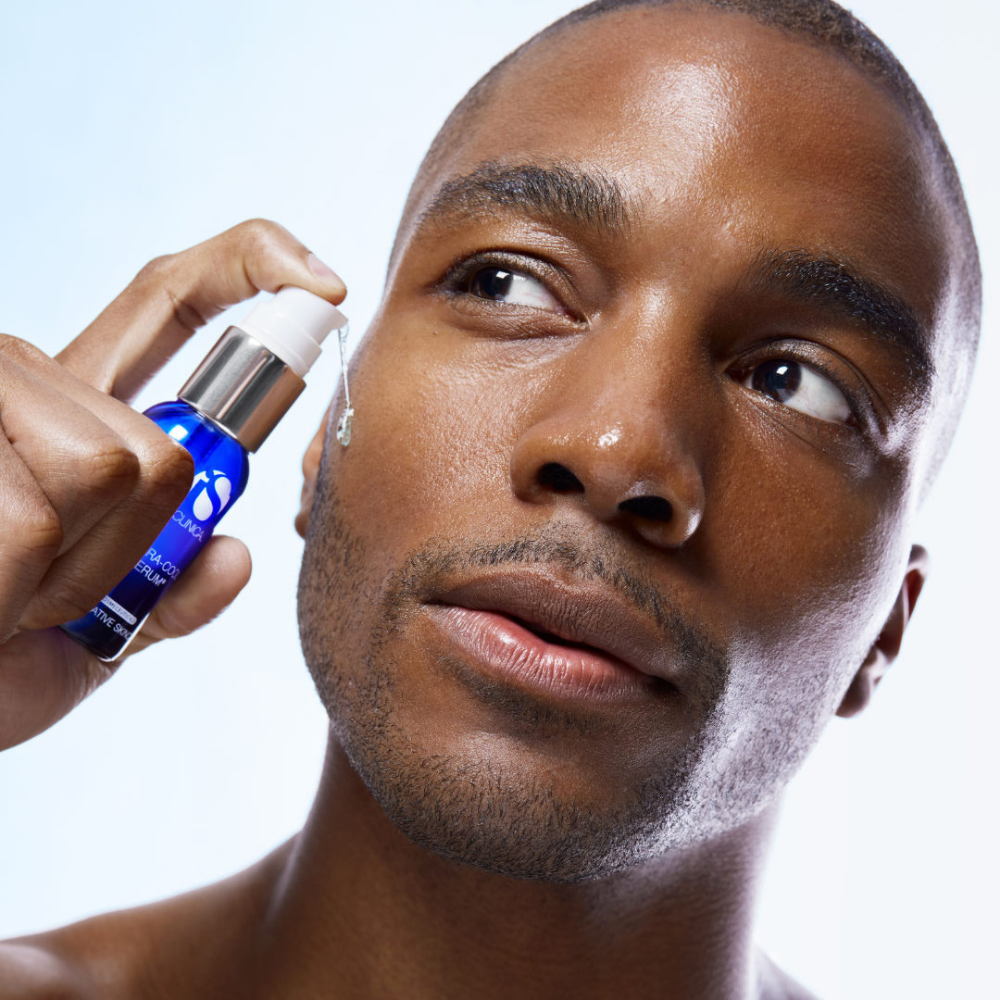 Man applying a blue spray of iS Clinical Hydra-Cool Serum to his face against a white background