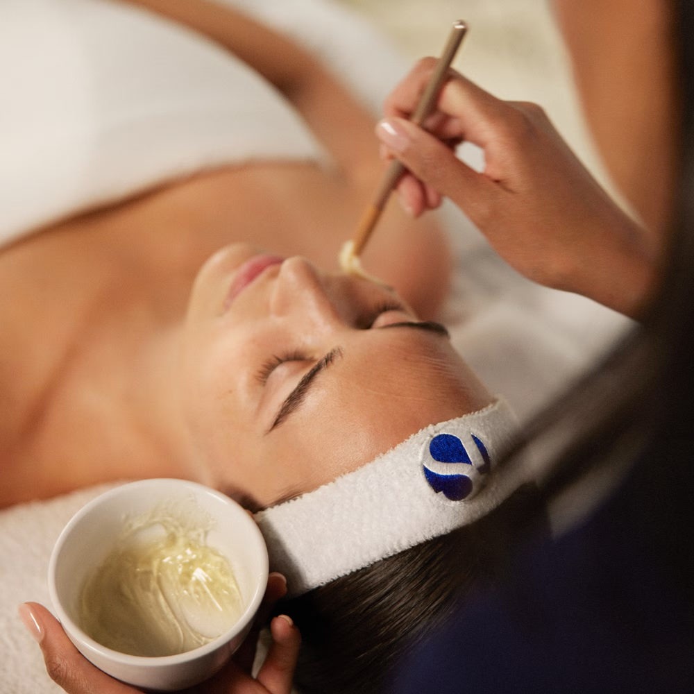 Woman receiving a facial treatment with a skincare professional applying iS Clinical Hydra-Intensive Cooling Masque to her face