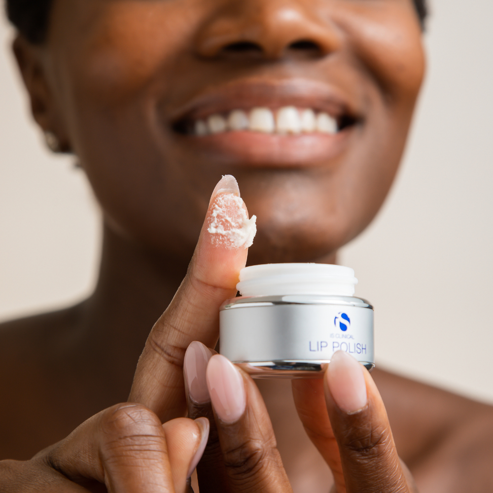 Person holding a container of 'Lip Polish' from the iS Clinical Lip Duo with a blurred background