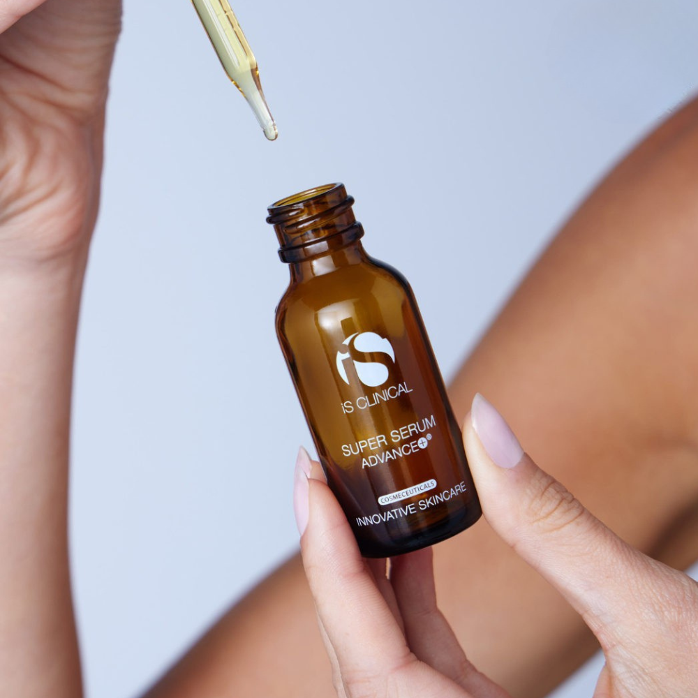 iS Clinical Pro-Heal Serum Advance+ with dropper held by a hand against a neutral background