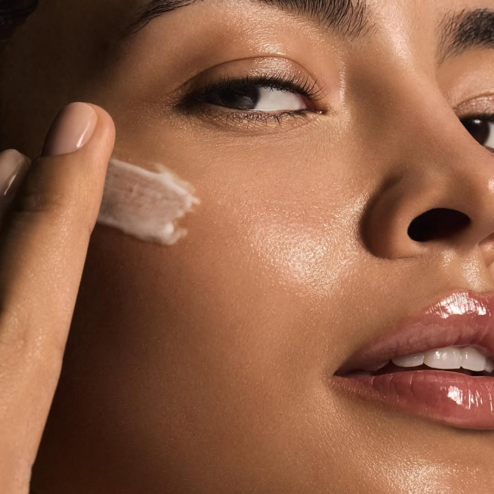 Close-up of a woman applying cream of iS Clinical Reparative Moisture Emulsion to her face with a finger
