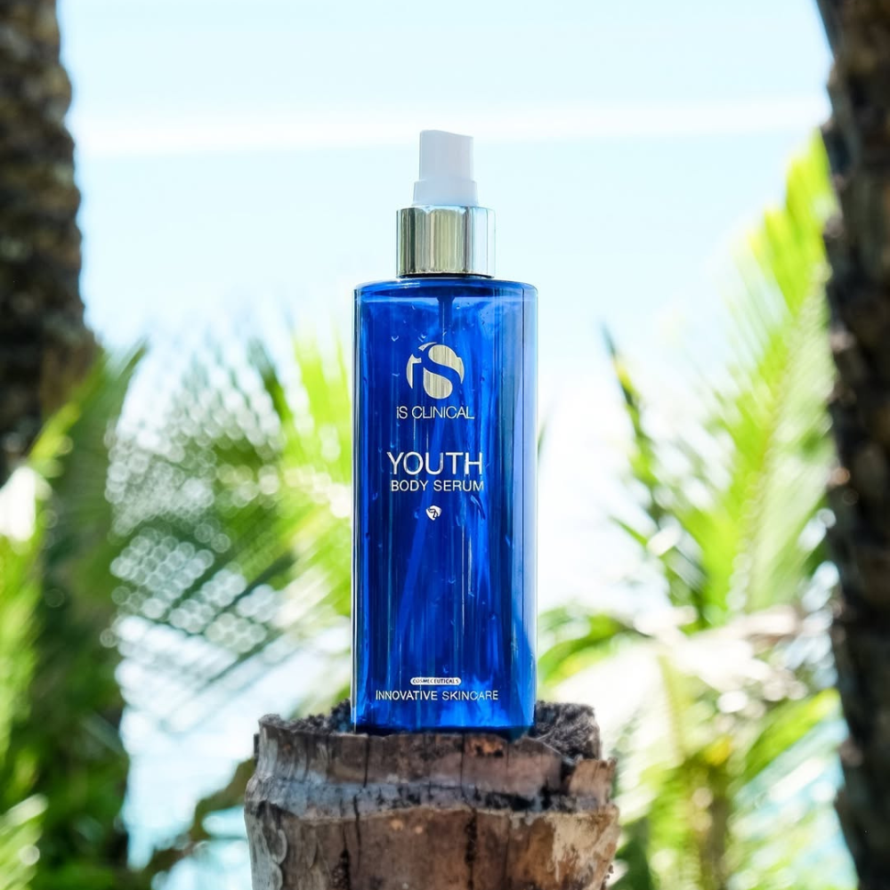Blue spray bottle of iS Clinical Youth Body Serum on a leafy background