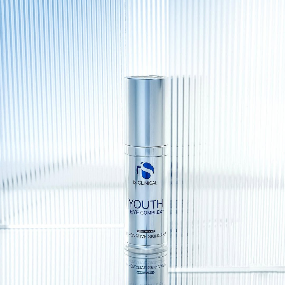 Skincare bottle labeled iS Clinical Youth Eye Complex on a textured light blue background