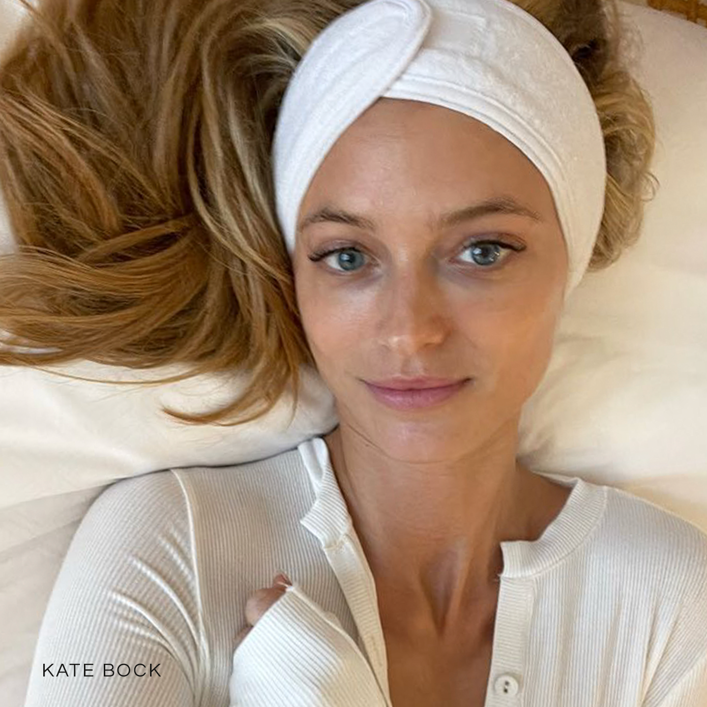 image of Kate Bock taking a selfie on a spa table, wearing a white spa head band and a while long sleeve shirt