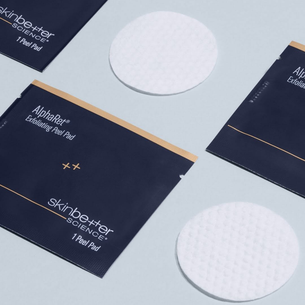 Skin Better AlphaRet Exfoliating Peel Pads cotton rounds and packaging laying on a light blue background
