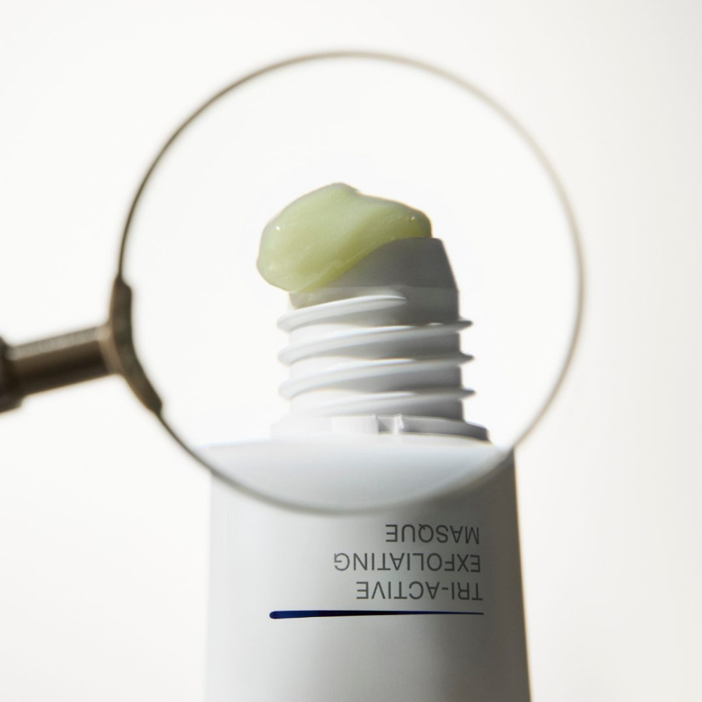 Close-up of a skincare product iS Clinical Tri-Active Exfoliating Masque with a magnifying glass showing a small amount of cream
