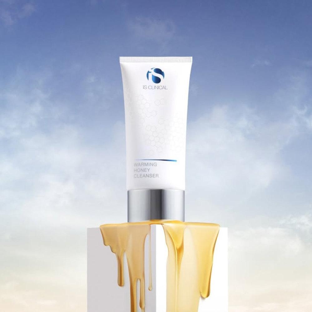 Tube of iS Clinical Warming Honey Cleanser on a podium with honey dripping down it on a blue and white sky background