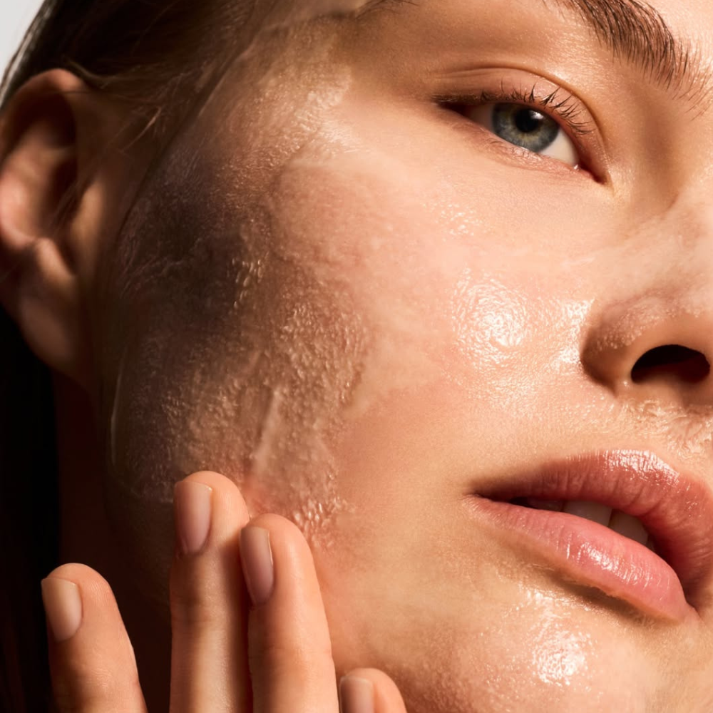 Close-up of a person's face with a hand gently touching the cheek, highlighting skin texture applying iS Clinical Warming Honey Cleanser