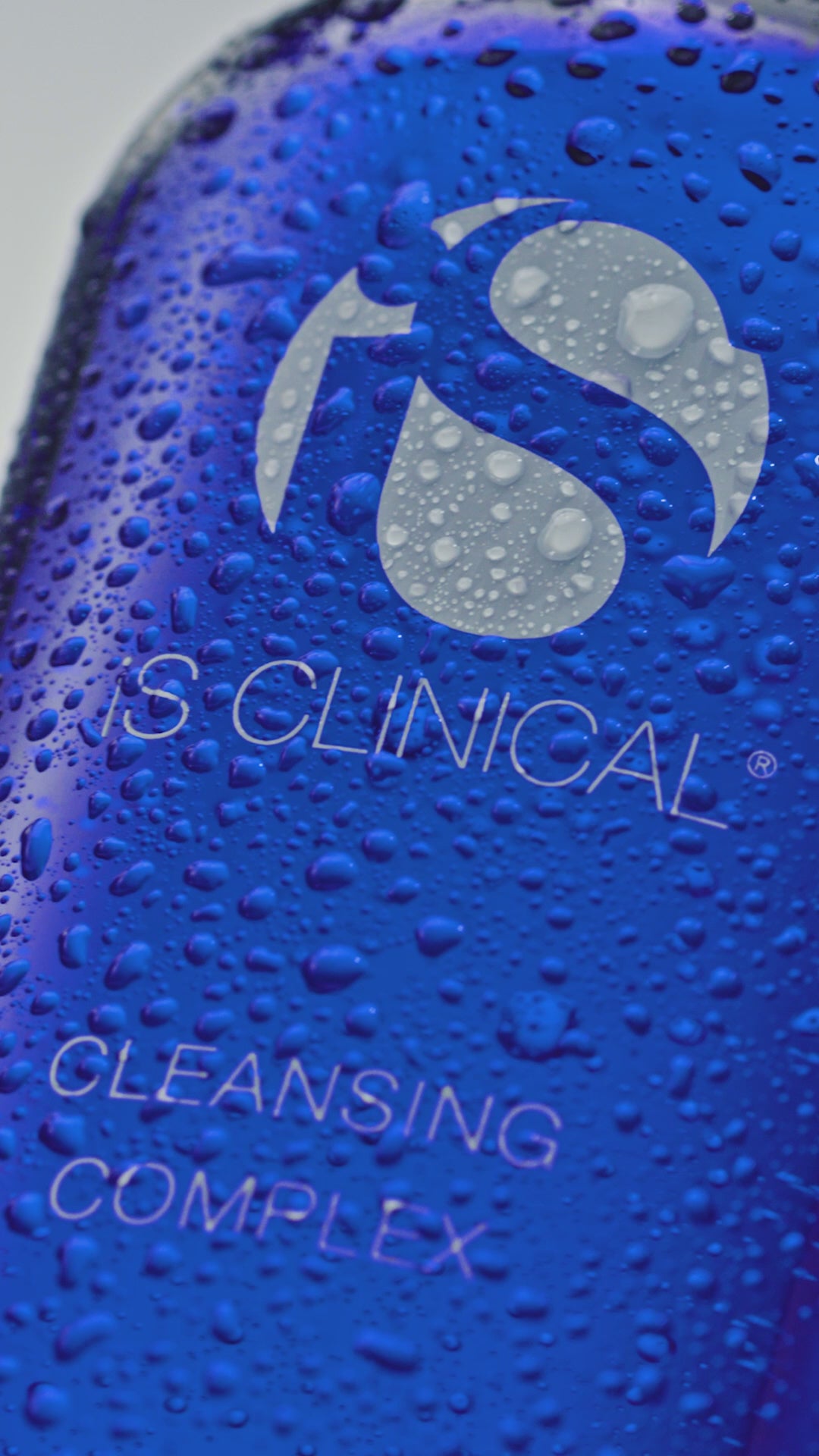Blue bottle of iS Clinical Cleansing Complex being poured into models hand and applied to the face while washing